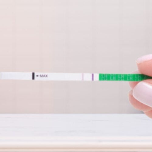 woman holding ovulation test in bathroom with faint line