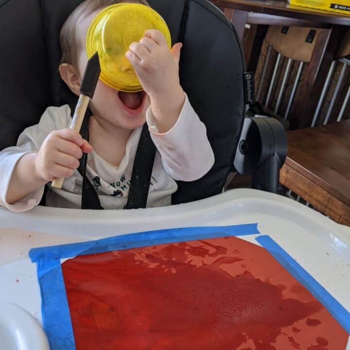 Toddler in high chair painting with water on contstruction paper.