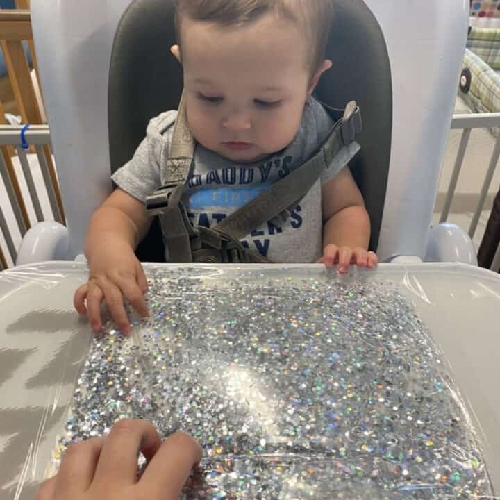 Toddler playing with glitter sensory bag in high chair
