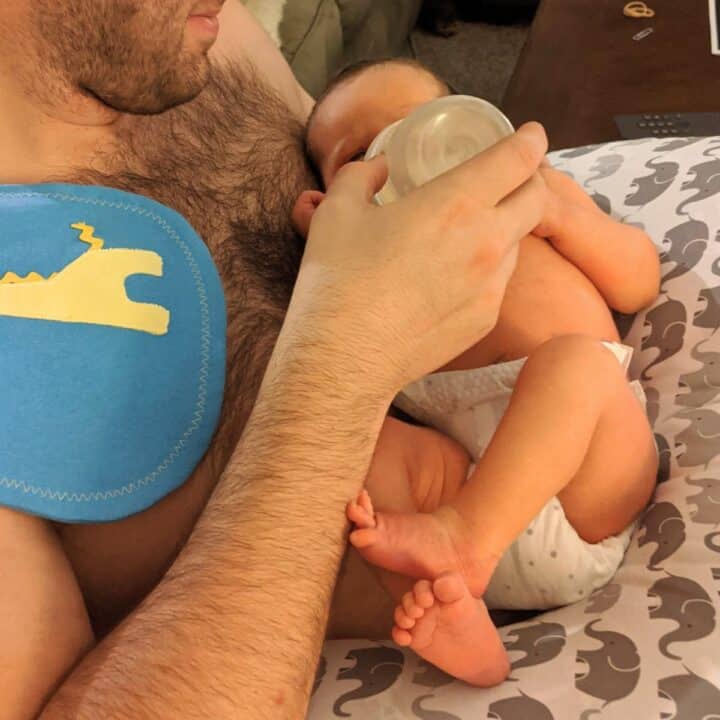 dad holding his newborn baby skin to skin giving a bottle with a burp cloth on his shoulder.